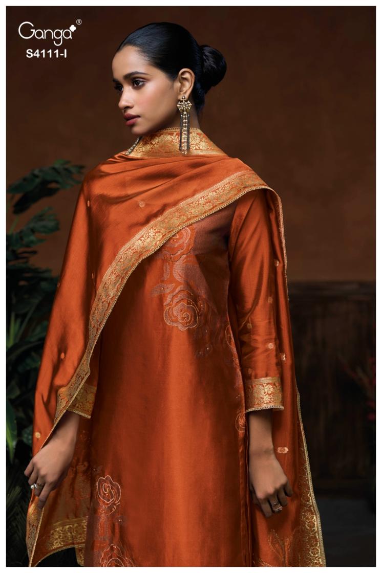 Woman wearing an orange traditional outfit with gold embroidery, branded 'Ganga'.